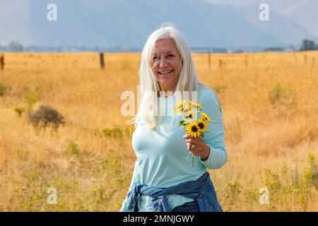 USA, Idaho, Bellevue, Porträt einer Seniorin mit einem Haufen Sonnenblumen Stockfoto