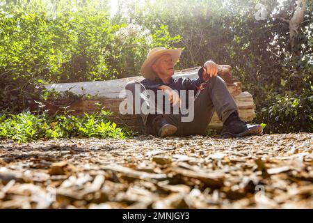 Ein älterer Mann ruht sich neben dem umgestürzten Baum aus Stockfoto