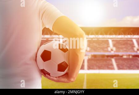 Gekürztes Bild von einem jungen Spieler, der im Stadion in Madrid einen Fußball unter den Armen hält, mit einem Sonnenuntergang im Hintergrund Stockfoto