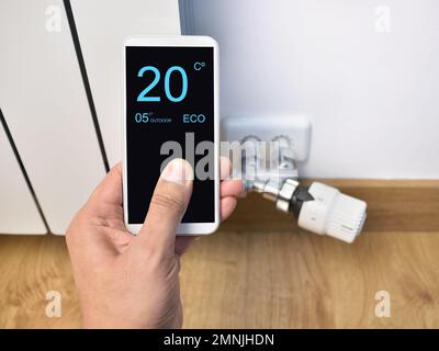 Nahaufnahme einer Person, die zu Hause die Temperatur mit dem Thermostat über ein Smartphone anpasst Stockfoto