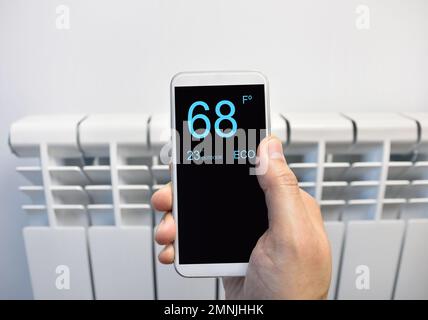 Nahaufnahme einer Person, die zu Hause die Temperatur mit dem Thermostat über ein Smartphone anpasst Stockfoto