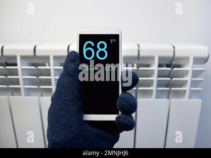 Nahaufnahme einer Person, die zu Hause die Temperatur mit dem Thermostat über ein Smartphone anpasst Stockfoto