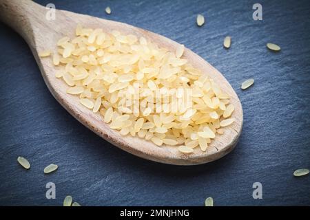 Brauner Reis auf Holzlöffel mit dunklem Stein Stockfoto