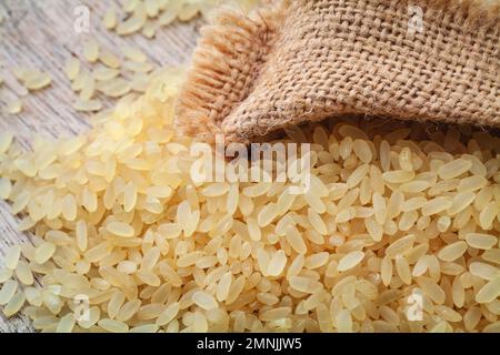 Braunes Reisgelb, für Risotto in Jute aus Leinensack auf einem Holzbrett Stockfoto