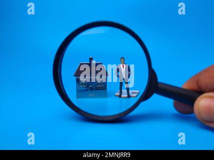 Miniaturmenschen, Schlüsselanhänger und Lupe auf blauem Hintergrund. Immobilienkonzept. Stockfoto