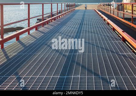 Fußgängerrampe zum Bootsanleger am See. Stahlrampe führt zur Bootsanlegestelle. Schwimmender Hafen im Wasser. Legen Sie an einem sonnigen Tag in einem See an. Straßenfoto, Sse Stockfoto