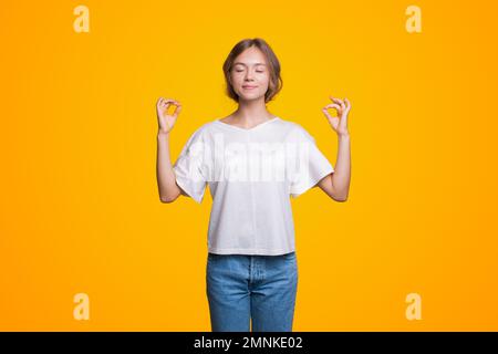 Friedlich entspannte Frau meditiert, atmet, frische Luft atmet Yoga, steht in Lotus nirvana Pose, isoliert auf gelbem Hintergrund. Stockfoto