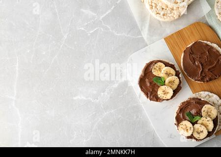 Gepuffte Reiskuchen mit Schokoladenaufstrich, Banane und Minze auf grauem Marmortisch, flach liegend. Platz für Text Stockfoto