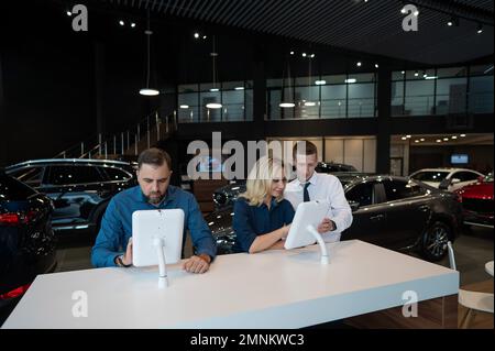 Kaukasisches Ehepaar wählt ein Auto in einem Autohaus auf digitalen Tablets. Stockfoto