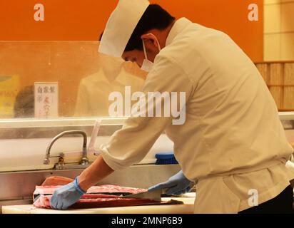 Sushi-Koch filetiert frischen Thunfisch im Kaiten Sushi Restaurant in Tokio, Japan. Stockfoto