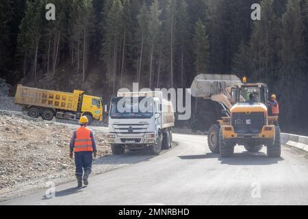 Schwere Baumaschinen mit Arbeitern arbeiten im Almaty-Gebirge. Bagger, Kipplaster und Arbeiter Stockfoto