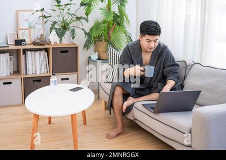 Der junge Mann, der zu Hause einen Computer benutzt Stockfoto