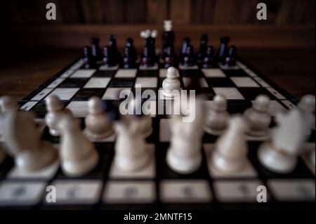 Verschwommener Hintergrund mit geringer Fokustiefe. Das Set aus Schachfiguren aus Holz, die auf einem Schachbrett auf dunklem Hintergrund stehen. Führung, Teamarbeit Stockfoto