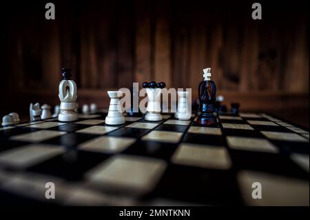 Verschwommener Hintergrund mit geringer Fokustiefe. Das Set aus Schachfiguren aus Holz, die auf einem Schachbrett auf dunklem Hintergrund stehen. Führung, Teamarbeit Stockfoto