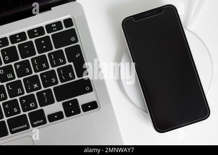 Flache Darstellung von Laptop und schwarzem Telefon auf kabellosem Ladegerät Stockfoto