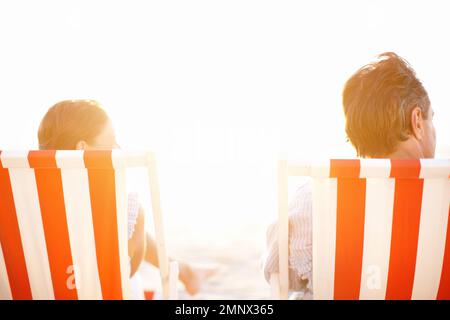 Wir baden zusammen in der Sonne. Ein reifes Paar, das einen wunderschönen Sonnenuntergang in Liegestühlen am Strand genießt. Stockfoto