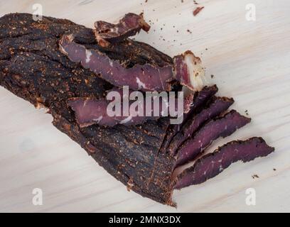 Frisch geschnittene südafrikanische Biltong mit selektivem Fokus auf heller Holzoberfläche Stockfoto