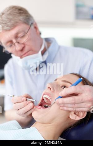 Für ein besseres Lächeln. Porträt eines reifen Arztes, der Frauenzähne überprüft. Stockfoto