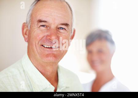 Gut aussehender reifer Mann, der mit einer Frau im Hintergrund lächelt. Porträt eines gut aussehenden, erwachsenen Mannes, der mit einer Frau im Hintergrund lächelt. Stockfoto