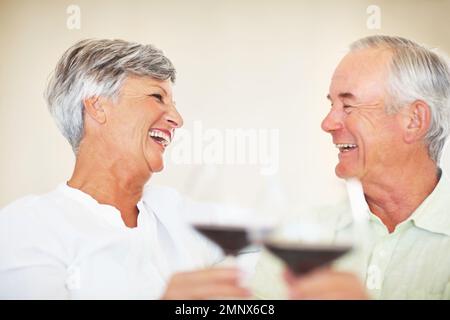 Wertvolle Momente. Fröhliches, reifes Paar, das zu Hause Zeit miteinander verbringt und Rotwein anstoßen möchte. Stockfoto