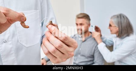 Audioprothetis nach Höruntersuchung bei hörgeschädigten Patienten wählen zwischen Ohrhörgeräten und Hörgeräten mit Ohrbügel zur Schwerhörigkeit Stockfoto