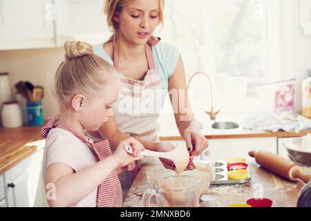 Sie bereiten ihren Kuchen für den Ofen vor. Süßes kleines Mädchen, das zu Hause mit ihrer mutter in der Küche backt. Stockfoto