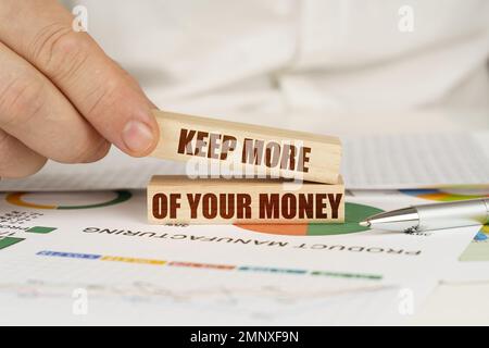 Geschäftskonzept. Auf dem Tisch befinden sich Geschäftsdiagramme und Diagramme in den Händen eines Holzblocks mit der Aufschrift „Keep More of Your Money“ Stockfoto