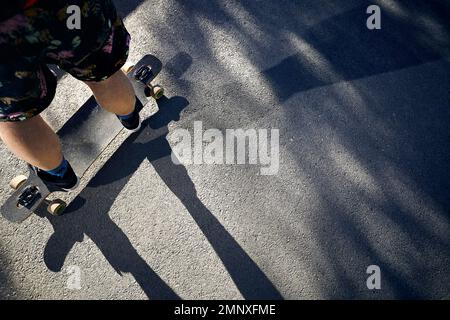 Man Skater auf seinem Longboard an der Mountain Road aus nächster Nähe bei hellem Sonnenlicht und rauem Schatten Stockfoto