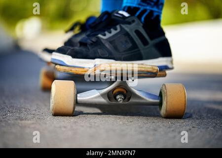 Man Skater auf seinem Longboard an der Mountain Road, Nahaufnahme bei hellem Sonnenlicht am Morgen Stockfoto