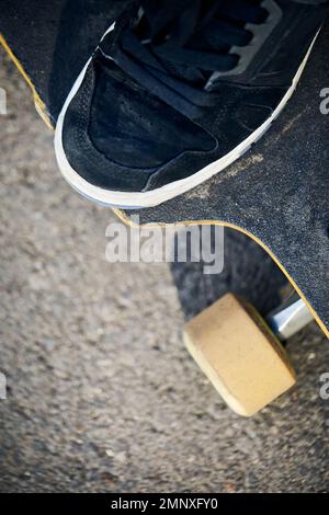 Man Skater auf seinem Longboard an der Mountain Road aus nächster Nähe bei hellem Sonnenlicht und rauem Schatten Stockfoto