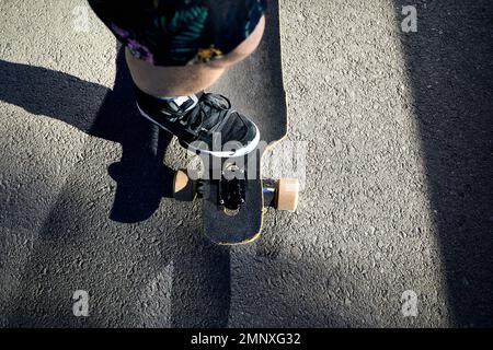 Man Skater auf seinem Longboard an der Mountain Road aus nächster Nähe bei hellem Sonnenlicht und rauem Schatten Stockfoto