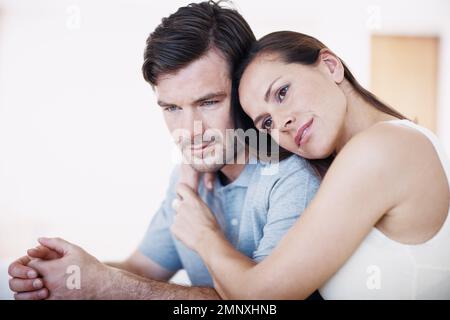 Es wird alles gut... Eine Frau, die ihren Mann umarmt, während er feierlich neben ihr sitzt. Stockfoto