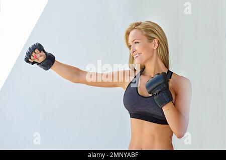 Der Tag beginnt mit Kickboxen. Eine sportliche junge Frau, die mit mma-Handschuhen trainiert. Stockfoto