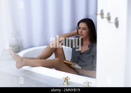 Lesen ist träumen mit offenen Augen. Eine junge Frau, die in der Badewanne ein Buch liest. Stockfoto