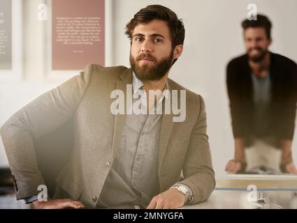 Der Erfolg hängt vom zweiten Buchstaben ab. Ein junger Geschäftsmann, der in seinem Büro mit seinem Kollegen sitzt, verschwommen im Hintergrund. Stockfoto