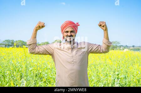 Glücklicher Feger zeigt mit zwei Händen auf dem Ackerland, indem er in die Kamera schaut – selbstbewusst, agrogeschäftlich und mit positiven Emotionen Stockfoto