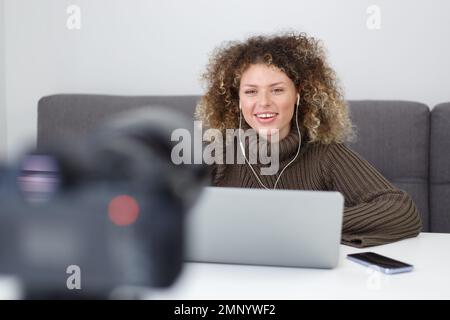 Video-Bloggerin, Frau, filmt zu Hause ein Bildungsprodukt. Freundliche weiße Frau mit lockigem Haar spricht auf Videokamera Stockfoto