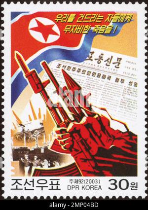 Nordkoreanische Propagandamarke aus dem Jahr 2003 mit Gewehr, Rakete, Nationalflagge und militärischen Slogans in koreanischer Schrift. Stockfoto