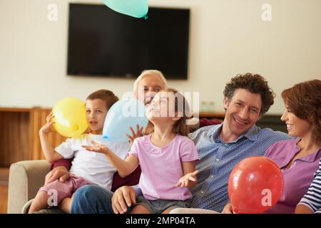 Alle Kinder mögen es. Ein Bruder und eine Schwester, die mit Ballons spielen, während sie bei ihrer Familie sitzen. Stockfoto