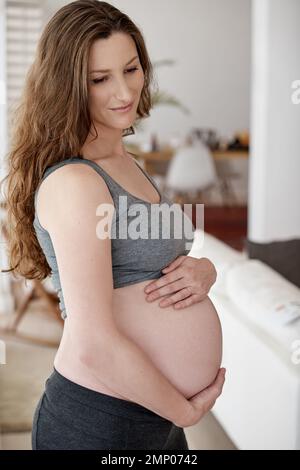 Große Dinge kommen in kleinen Paketen. Eine junge schwangere Frau, die in ihrem Haus steht. Stockfoto