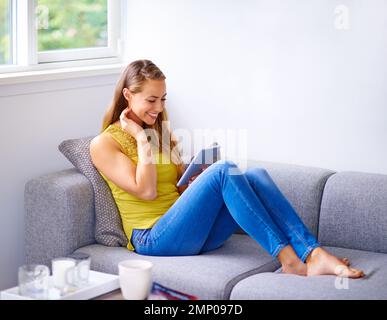 Ich schaue mich auf der Couch gemütlich um. Eine junge Frau, die zu Hause ein Tablet auf ihrem Sofa benutzt. Stockfoto