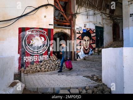 Ein Mann, der in der Nähe von Wandbildern von Fußball und Revolution in der Kasbash, Nordafrika, Algier, Algerien vorbeikommt Stockfoto