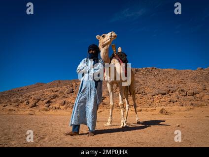 Tuareg-Mann steht vor seinem Kamel in der Wüste, Nordafrika, Tamanrasset, Algerien Stockfoto