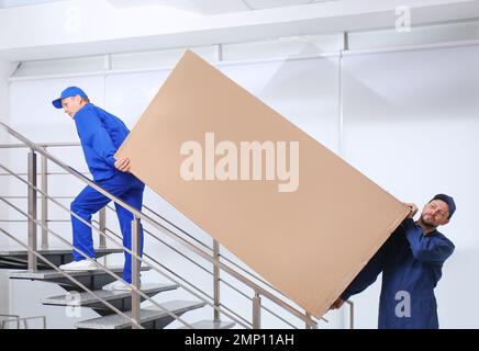 Professionelle Arbeiter, die Kühlschränke auf Treppen in Gebäuden tragen Stockfoto
