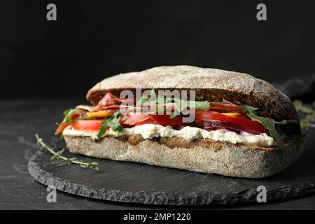 Köstliches Sandwich mit frischem Gemüse und Prosciutto auf dem schwarzen Tisch Stockfoto