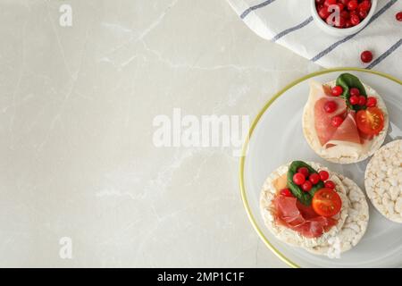 Gepuffte Reiskuchen mit Prosciutto, Beeren und Basilikum auf grauem Marmortisch, flach liegend. Platz für Text Stockfoto