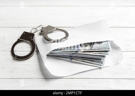 Dollarscheine und Handschellen auf weißem Holztisch. Bestechungskonzept Stockfoto