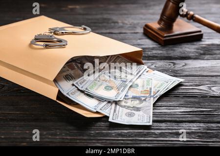 Umschlag mit Dollarscheinen und Handschellen auf schwarzem Holztisch. Bestechungskonzept Stockfoto