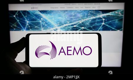 Person, die ein Mobiltelefon mit dem Logo des australischen Energiemarktbetreibers (AEMO) auf dem Bildschirm vor der Webseite hält. Konzentrieren Sie sich auf das Display des Telefons. Stockfoto