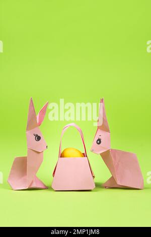 Oster-Origami - zwei Papierhasen und ein Ei mit grünem Hintergrund. Basteln für die Feiertage, machen Sie es selbst. Stockfoto